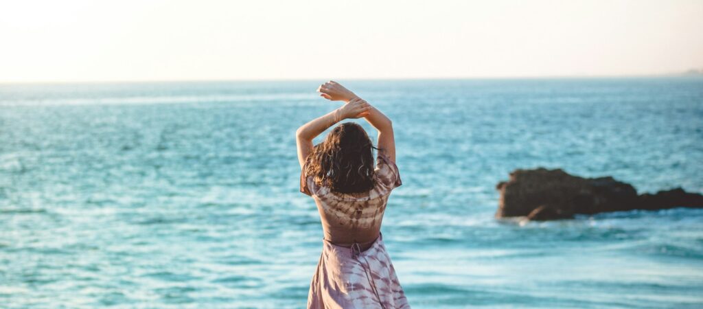 Frau am Meer in entspannter Haltung – Sinnbild für Ruhe, Zyklus verstehen und hormonelle Balance im Online-Programm ZYKLUS Kompass